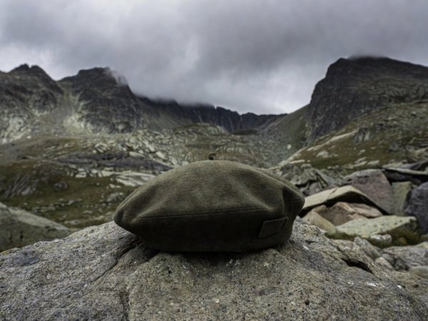 Dark olive tactical felted wool beret resting on a granite rock during a mountain wilderness expedition